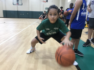 Co-ed basketball summer camp girl focused dribbling one basketball.